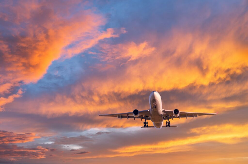 Airplane is flying in colorful sky at sunset. Passenger airplane